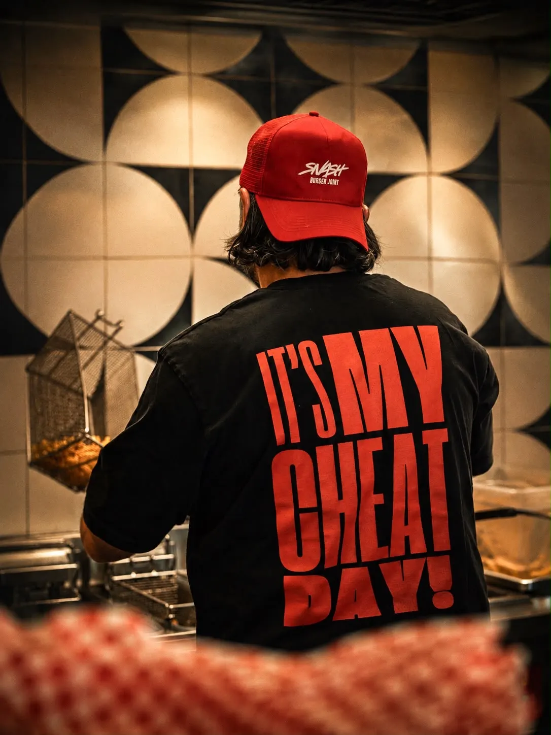 Mitarbeiter an der Fritteuse, Rückenaufdruck „It's my cheat day“